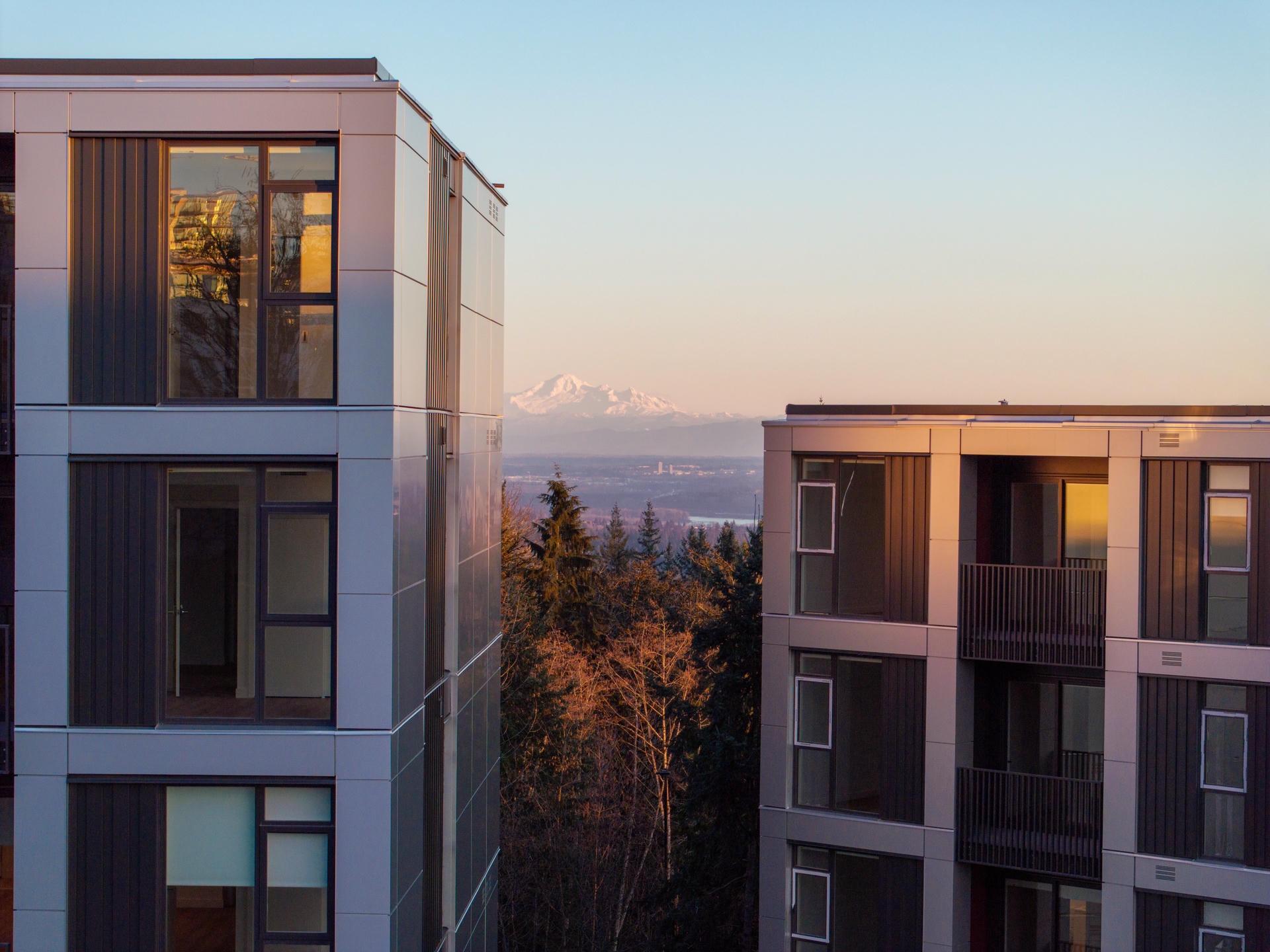 Exterior view of Koto in Burnaby, featuring modern architecture framed by sweeping mountain views under a clear sky.